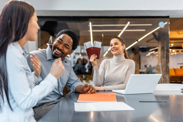 Young cute couple choosing a trip with agent sitting at the travel agency office holding two possports.